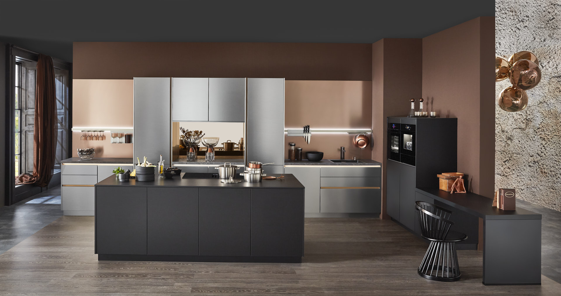 Hauptschuss, Mix aus Keramik und Bronzenachbildung, Kücheninsel mit Bosch Induktionskochfeld und Muldenlüfter, schwarzer Schrank, Edelstahlfronten, Bronze Nischenrückwand, 2 Bosch Einbaubacköfen, Messing Spüle