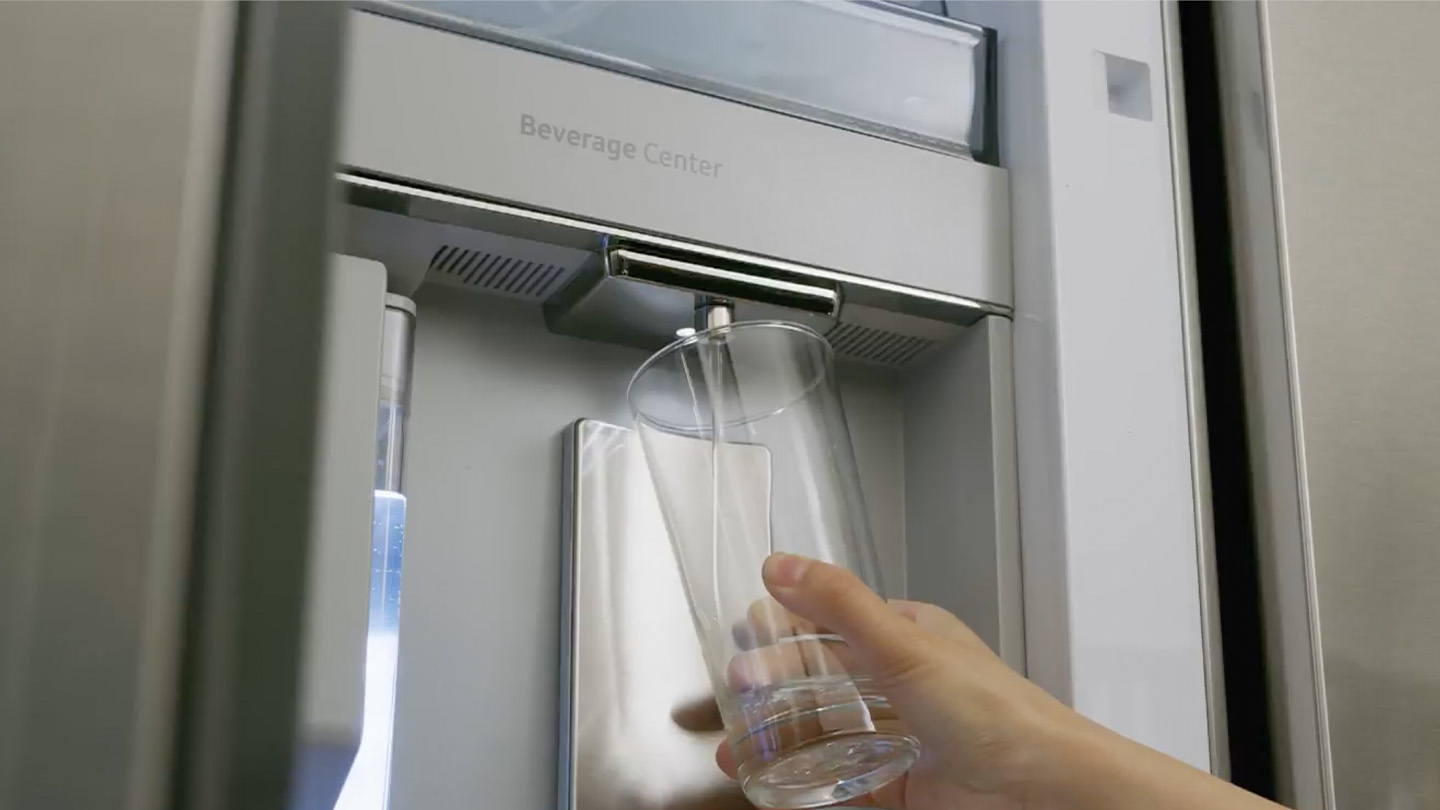 Hand mit Glas unter in Kühlschrank integrierten Wasserspender