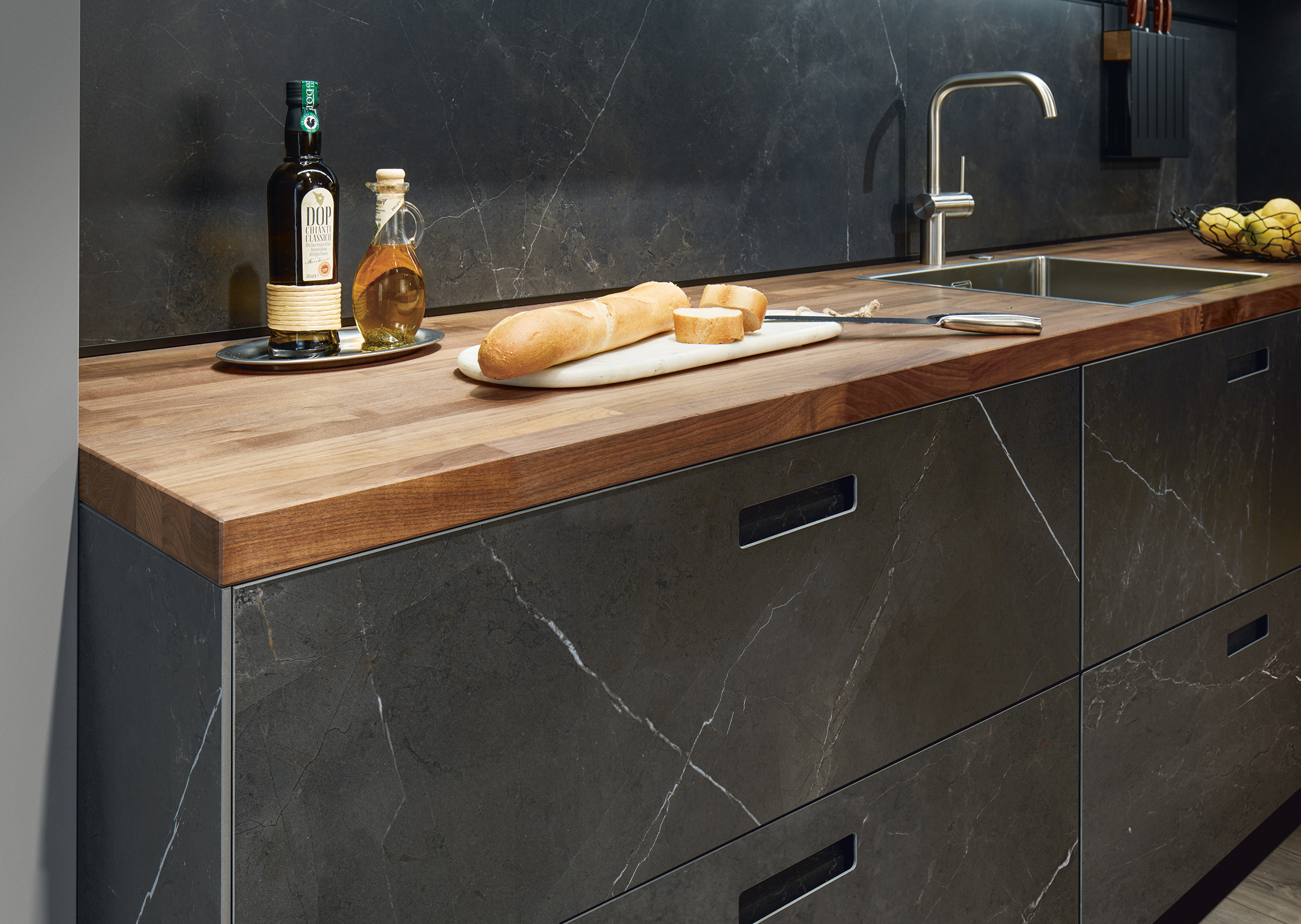 systemo Massivholzarbeitsplatte integrierte Edelstahlspüle Quarzstein-Küchenfronten und Nischenrückwand Holzbrett darauf mit Baguette und Brotmesser