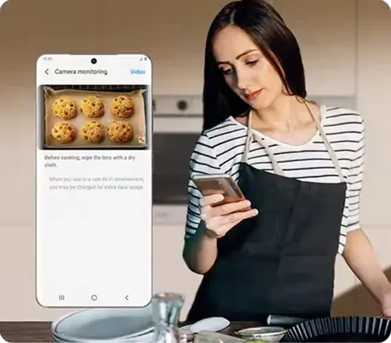 Frau mit Backschürze blickt auf Handy mit Back-App